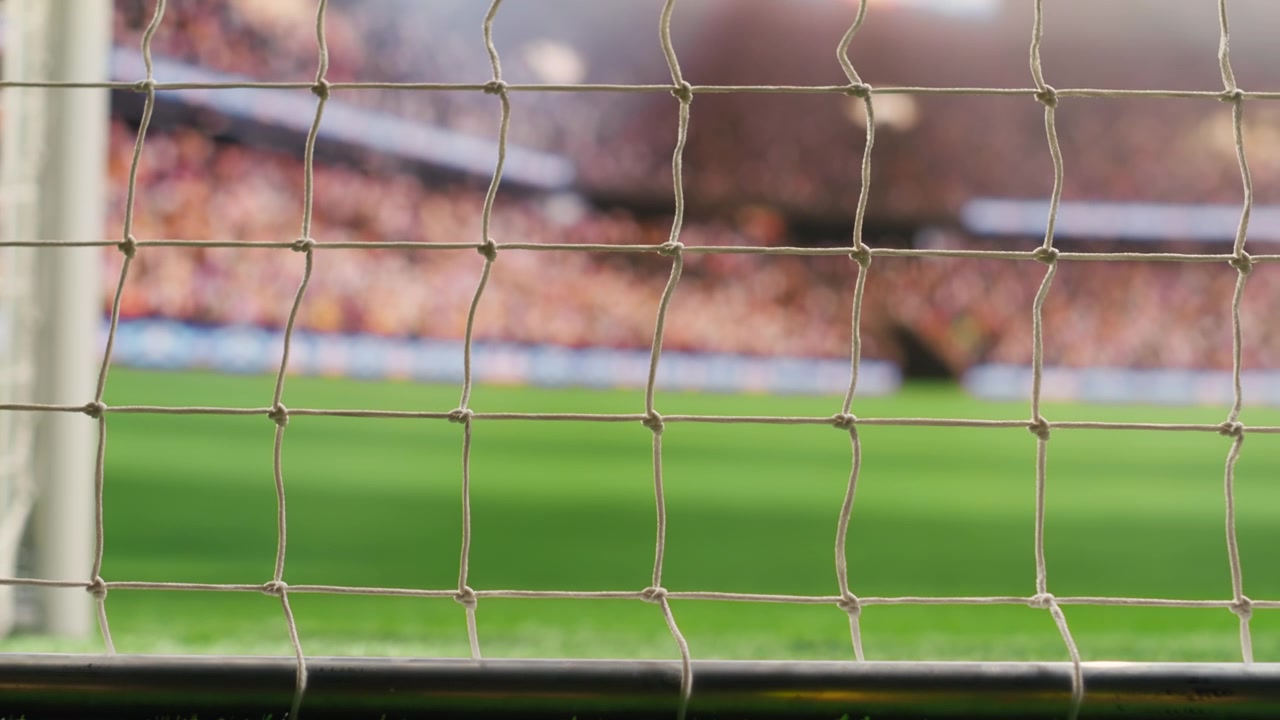 Stort fotbollsmål med nät och stolpar mot tom plan med suddig stadionpublik