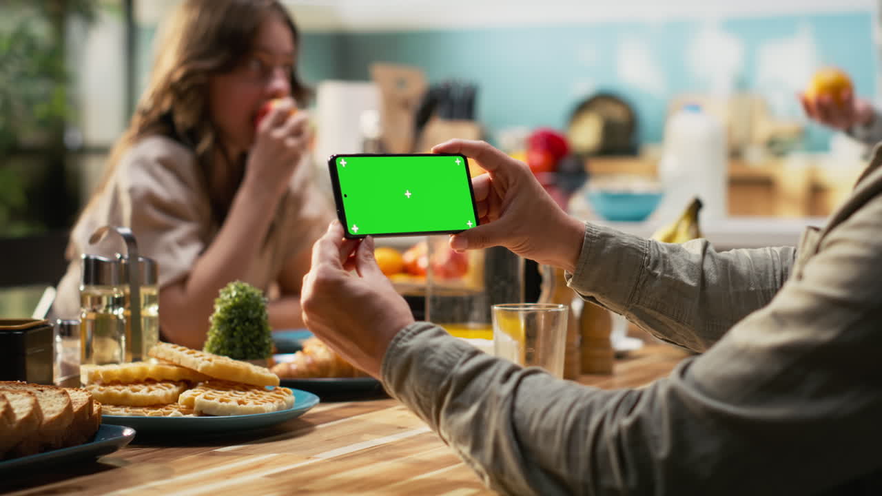 Chroma key on phone next to family enjoying breakfast at the kitchen table