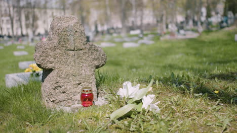 cross tombstone with a white flower and a grave candle on the grass in a graveyard on a sunny day 1