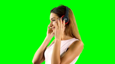 una rubia sonriente disfruta escuchando música en auriculares con fondo verde
