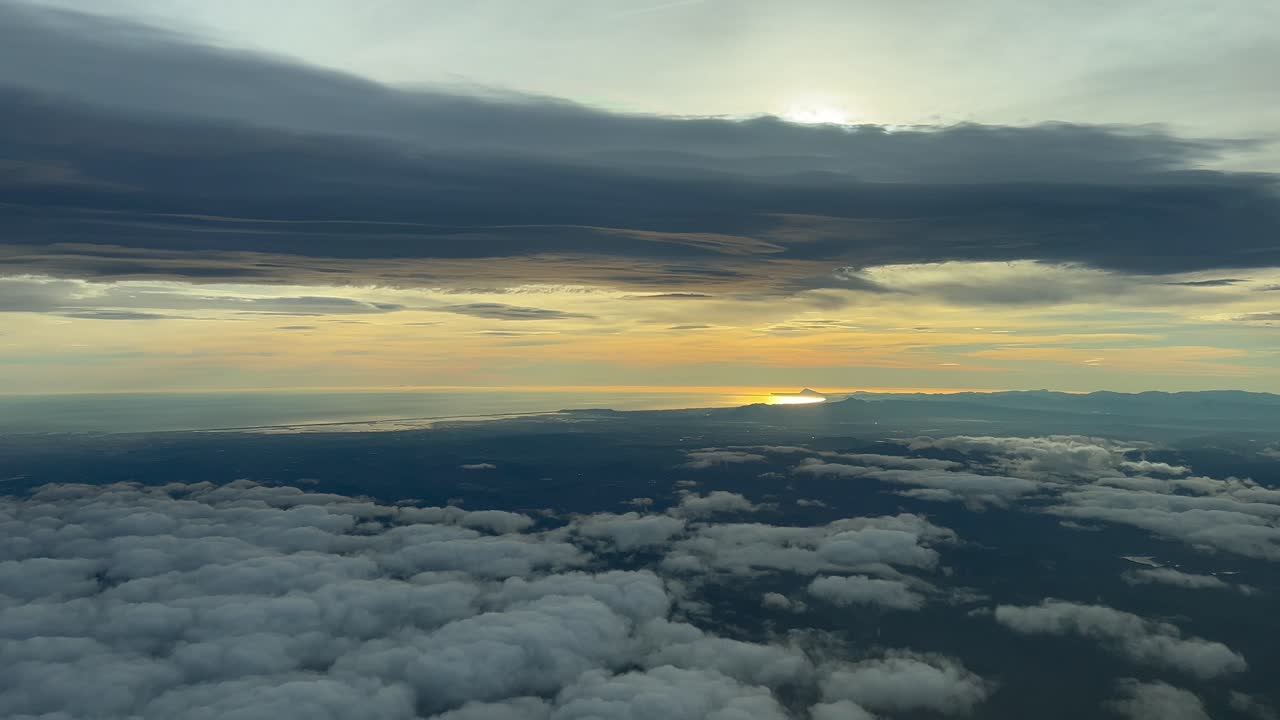 일몰 때 서쪽으로 날아가는 비행기 객실에서 찍은 발렌시아 시와 해안의 화려한 공중 전망, 태양은 회색 구름에 가려져 있습니다.