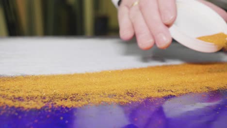 slowmotion of man covering blue glass-plate with yellow powder for glass fusing