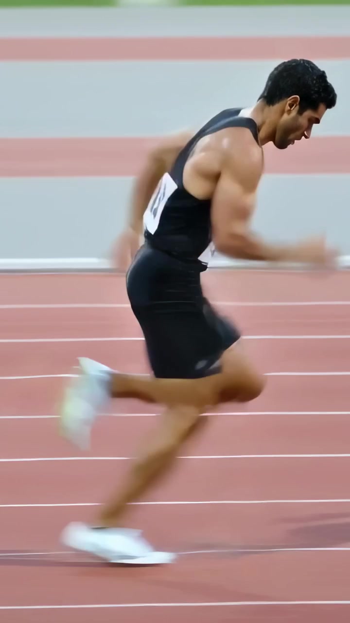 Vídeo vertical: Sprinter largando ao tiro, impulsionando-se dos blocos em pista vermelha, com regata preta e número de peito.