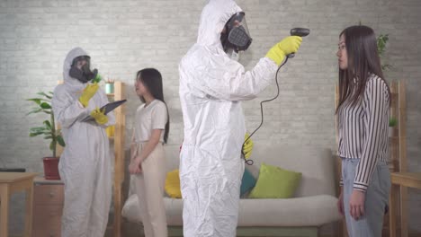 epidemiólogos en trajes de protección miden la temperatura de las niñas asiáticas en casa