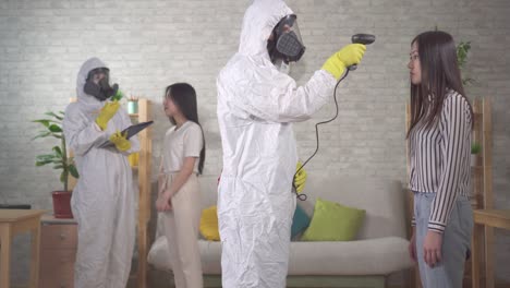 epidemiologists in protective suits measure the temperature of asian girls at home