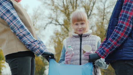 child volunteer collects trash in the park smiling at the camera