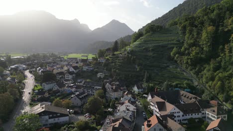 Aerial-shot-of-a-city-situated-in-the-valley-surrounded-by-mountains-with-dense-forest-in-swizz-alps