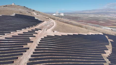 Drohnenaufnahme-Von-Solarpark-Panels,-Hügeln,-Kohlekraftwerk,-Hintergrund,-Blauer-Himmel