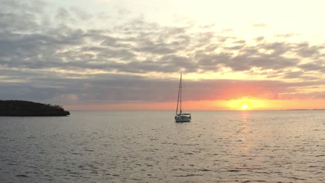 person swinging on hammock on a sailboat floating in the ocean at sunset. - aerial pullback