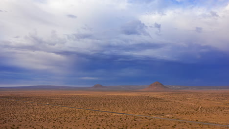 Aerial-hyperlapse-of-the-Mojave-Desert-landscape,-mountain-peaks-and-traffic-moving-along-a-straight-highway