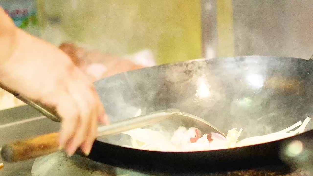 Close-up of a chef stir-frying onions and eggs in a hot wok over a flame.