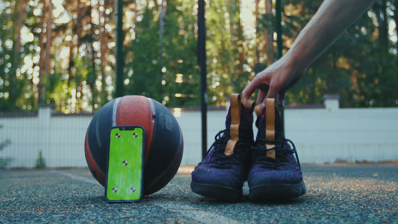 Green screen phone mock-up with tracking markers, basketball ball and sports shoes on court. Chroma key smartphone