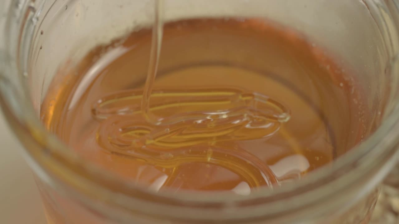 Miele dorato liquido e trasparente che gocciola in un barattolo, primo piano