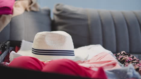 little girl hand puts straw hat into suitcase on sofa