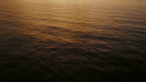 orange sunset, sunlight over calm ocean wave ripples in costa rica - aerial drone shot