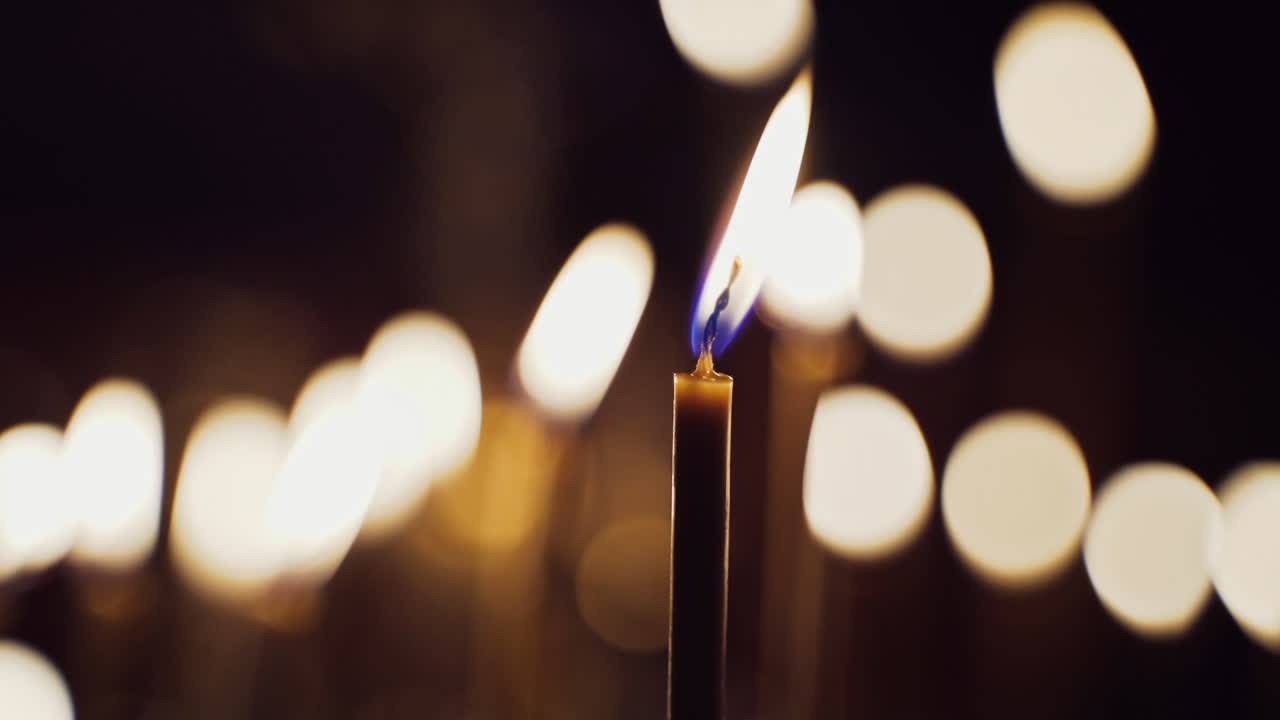 Uma vela queimando intensamente sobre luzes desfocadas. Velas acesas para intenções de oração em um templo noturno. Close-up.