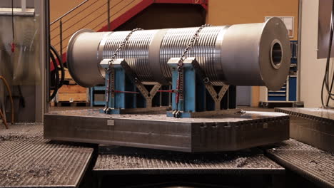 Rotating big metal cylinder chained down on machine at workshop