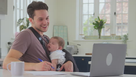 Transgender-Father-Working-From-Home-On-Video-Call-On-Laptop-Looking-After-Sleeping-Baby-In-Sling