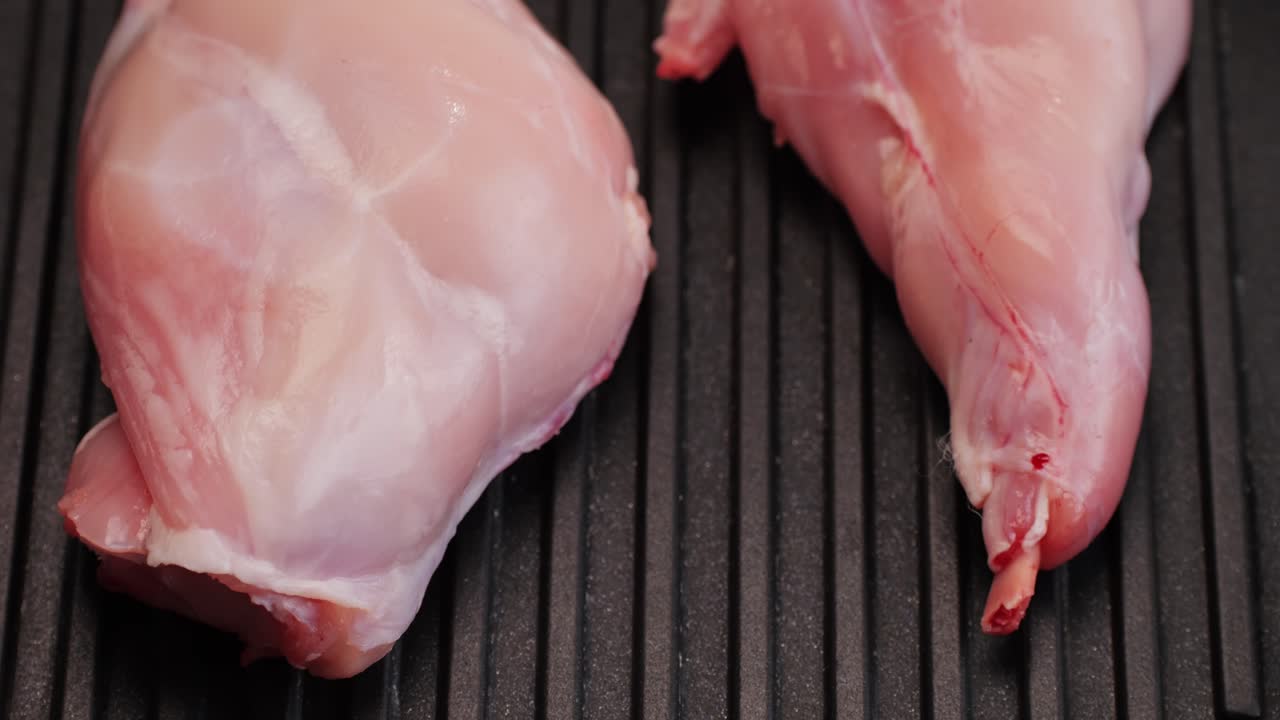 Roasted rabbit legs in a grill pan, healthy diet meat close up, chef cooking rabbit on kitchen restaurant, Black background. Top view