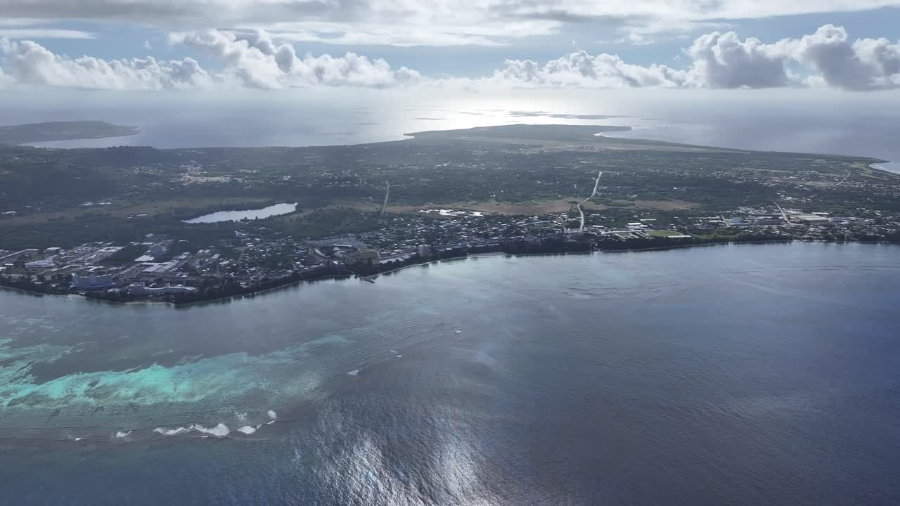 "A stunning aerial drone shot capturing the calm and crystal-clear emerald waters of Saipan’s west coast. Features beautiful coral reefs visible through the transparent sea."
