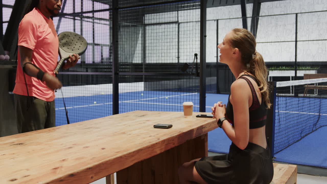 Diverse athletes preparing for padel tennis match, checking smartphones at indoor court