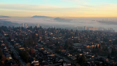 Atemberaubender-Sonnenuntergangsnebel-über-Häusern-Und-Mietwohnungen-In-Der-Nachbarschaft-Von-North-Vancouver-In-Kanada-–-Drohnenantenne,-Die-Vorwärts-In-Den-Himmel-Fliegt,-Zarte-Wolken-Und-Orangefarbene-Blaugrünfarben,-SFU-Und-Mount-Baker,-In-UHD