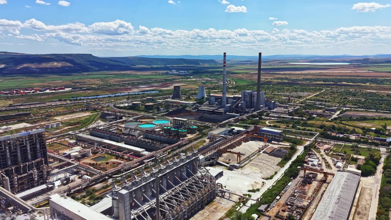 Gündüz vakti, açık bir gökyüzü altında, enerji santralleri ve çevresindeki manzaraya sahip bir sanayi sitesi görünümü.