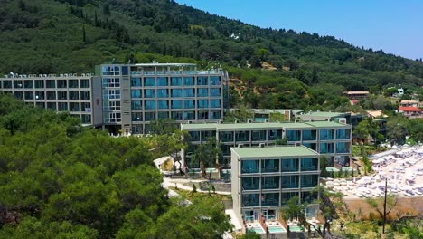 Beautiful-total-view-tracking-shot-at-the-coastline-of-Greece,-Europe,-hotels,-trees,-pool,-beach,-sea,-no-people,-daylight,-a-sunny-day,-blue-sky