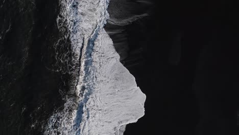 aerial top down shot of black basalt beach with sunlight