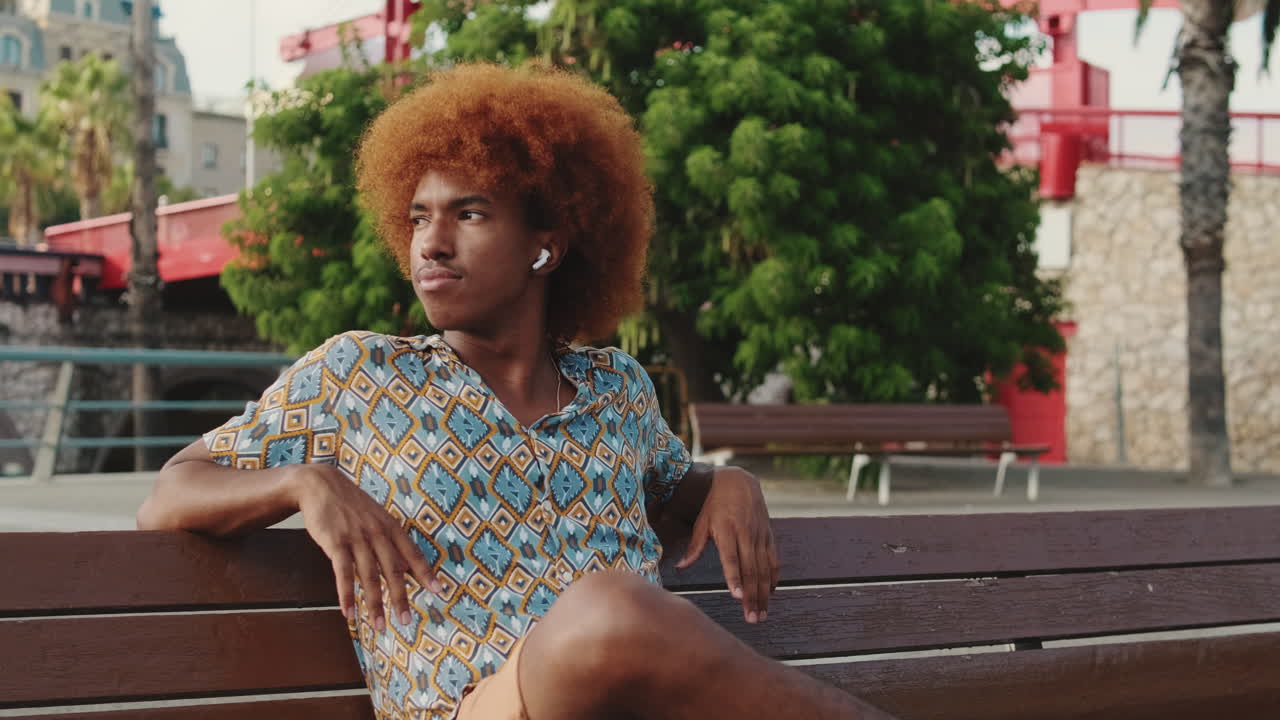 Young Man with Afro Hair Sitting on a Bench Outdoors