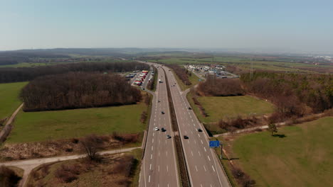 Forwards-reveal-highway-rest-area-with-petrol-station-at-multilane-highway.-Aerial-view-of-cars-and-trucks-driving-on-straight-motorway.-Traffic-and-transportation-concept.