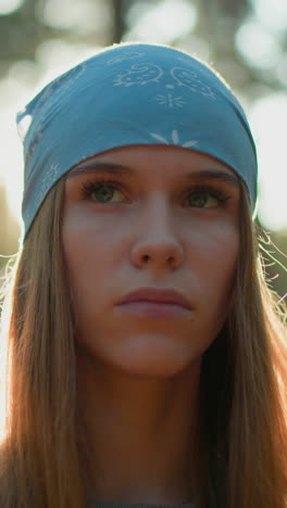 joven con pañuelo azul está de pie en el bosque, mirando intenso y contemplativo como la luz del sol crea un resplandor radiante alrededor de su cara y efecto alrededor del fondo