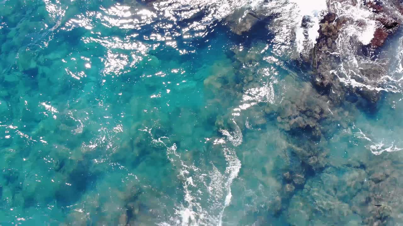 una gran sombra negra en forma de pez se mueve a través de las olas cerca de acantilados volcánicos en la isla de hawai