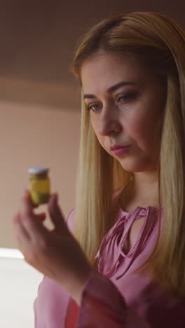 thoughtful lady in pink blouse looks at cyanide powder in bottle planning murder or suicide in kitchen at home close view slow motion