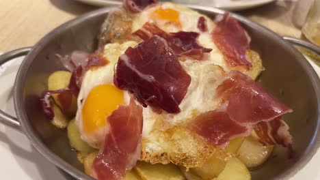 national spanish tapa with iberian ham, eggs, and potatoes in a pan at a restaurant in spain, traditional breakfast dish, 4k shot