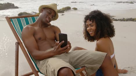 hombre afroamericano mostrando fotos a una mujer en un teléfono móvil en la playa 4k