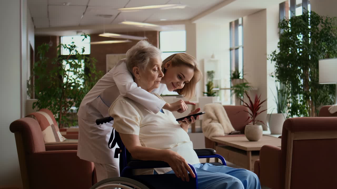 Caregiver Showing Smartphone to Elderly Woman in Wheelchair