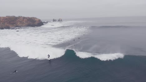 Aerial-shot-following-surfer-riding-foam-wave-at-Pichilemu,-Chile