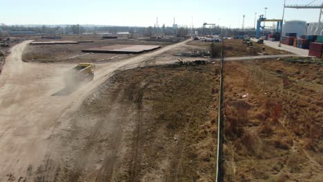 Drone-shot-following-a-dump-truck-at-a-construction-site-near-port