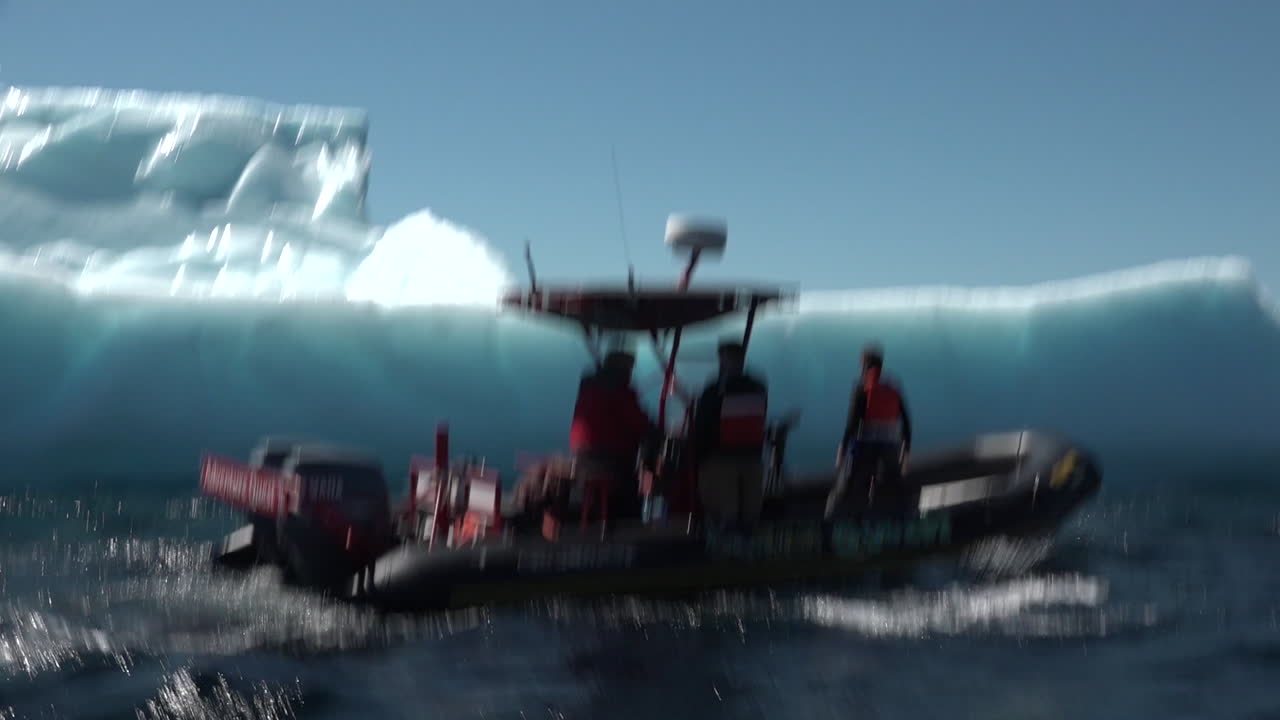 조디악 보트의 남자들이 북극에서 거대한 빙산을 통과합니다.