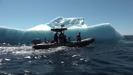 los hombres en un bote del zodiaco pasan un iceberg enorme en el ártico