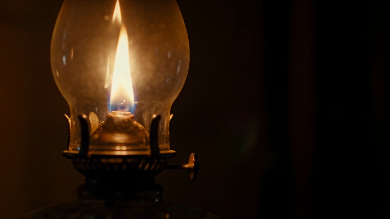 Stoppino di una lampada a olio antica che brucia, la fiamma tremola e poi si riduce a un bagliore blu, a supporto di uno studio di storia.