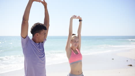 young biracial man and caucasian woman stretch on a sunny beach