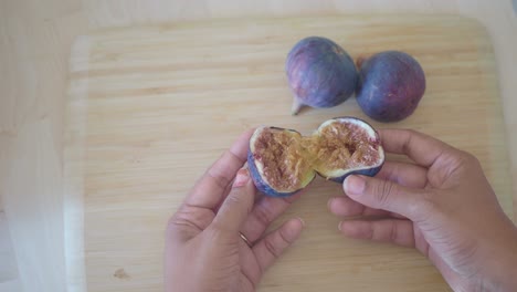 hands splitting open a fresh fig on a cutting board