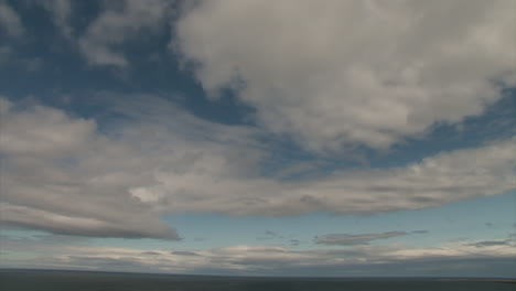 time lapse of light clouds moving away from camera across blue sky over flat landscape without trees in iceland