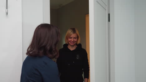 massage therapist in navy uniform opens door with warm smile to welcome client who smiles back in bright white treatment room, creating friendly, professional atmosphere before relaxation session