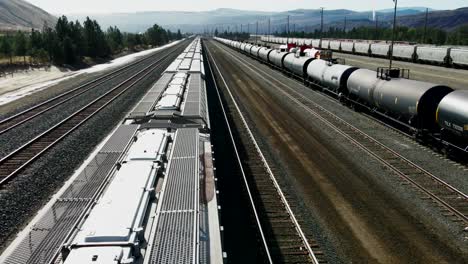 forward-flight-dolly-drone-shot-flying-close-over-a-cargo-train-on-a-railroad-station-in-a-desert-environment-on-a-sunny-day-with-mountains-in-the-background-and-powerlines-and-tank-trains