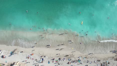 overhead aerial of crystal clear blue waters as waves crash and people on vacation enjoy family time in the sun and sand