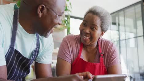 Glückliches-Afroamerikanisches-Seniorenpaar,-Das-Zusammen-Kocht-Und-Ein-Tablet-In-Der-Küche-Verwendet