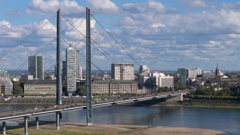 Rhine-Knee-bridge-with-Dusseldorf-Skyline,-telephoto-drone-establishing-shot,-sunny-day-fair-weather-cumulus